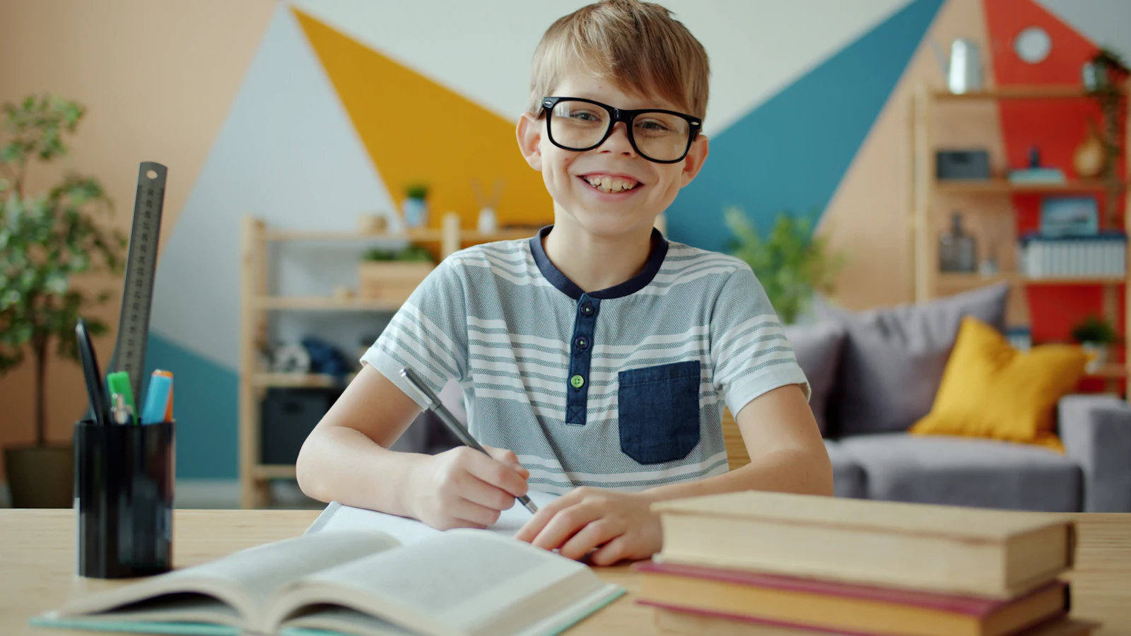 Un écolier à lunettes sourit en faisant ses devoirs dans une pièce colorée