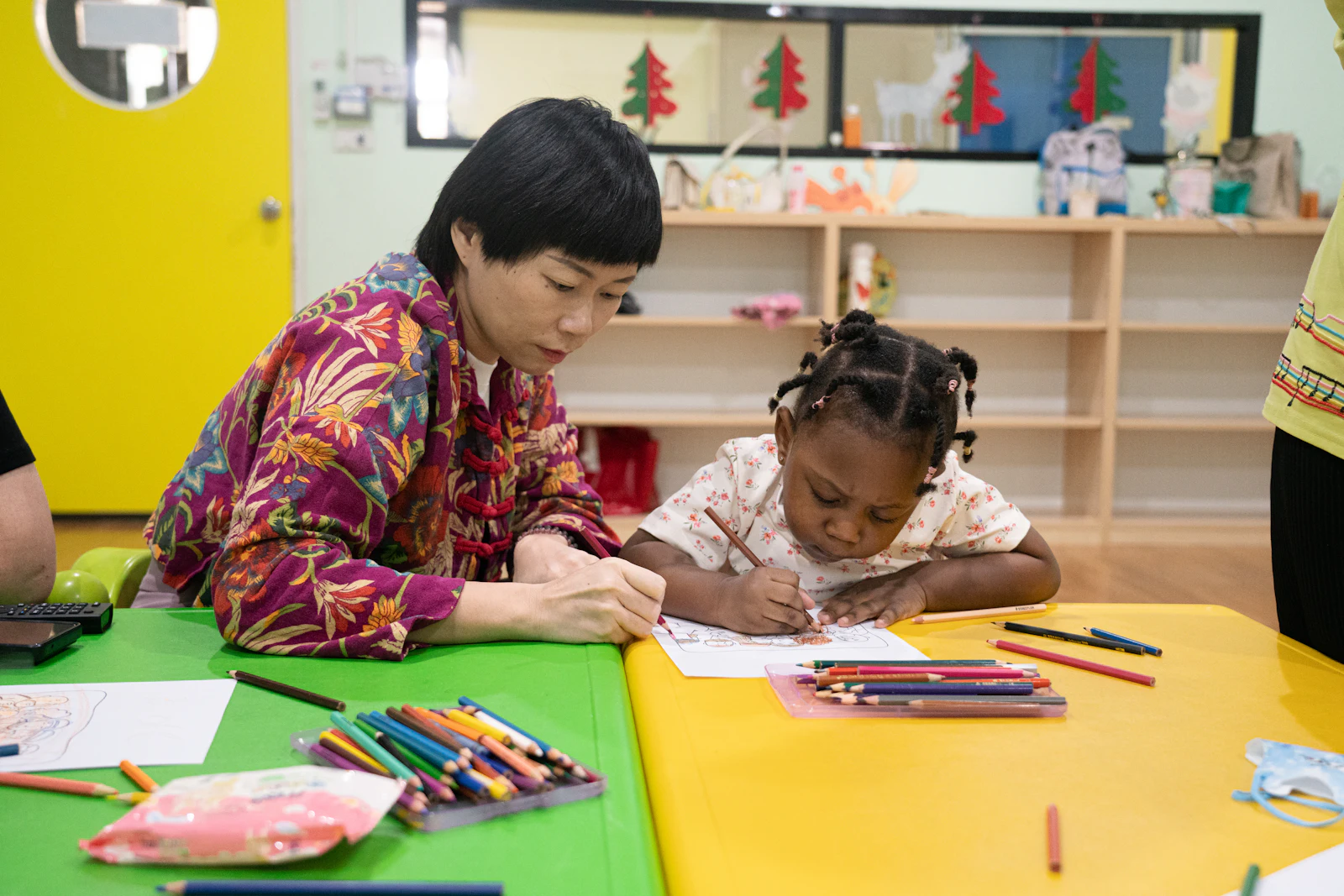 Une éducatrice dessine avec un enfant dans une salle colorée