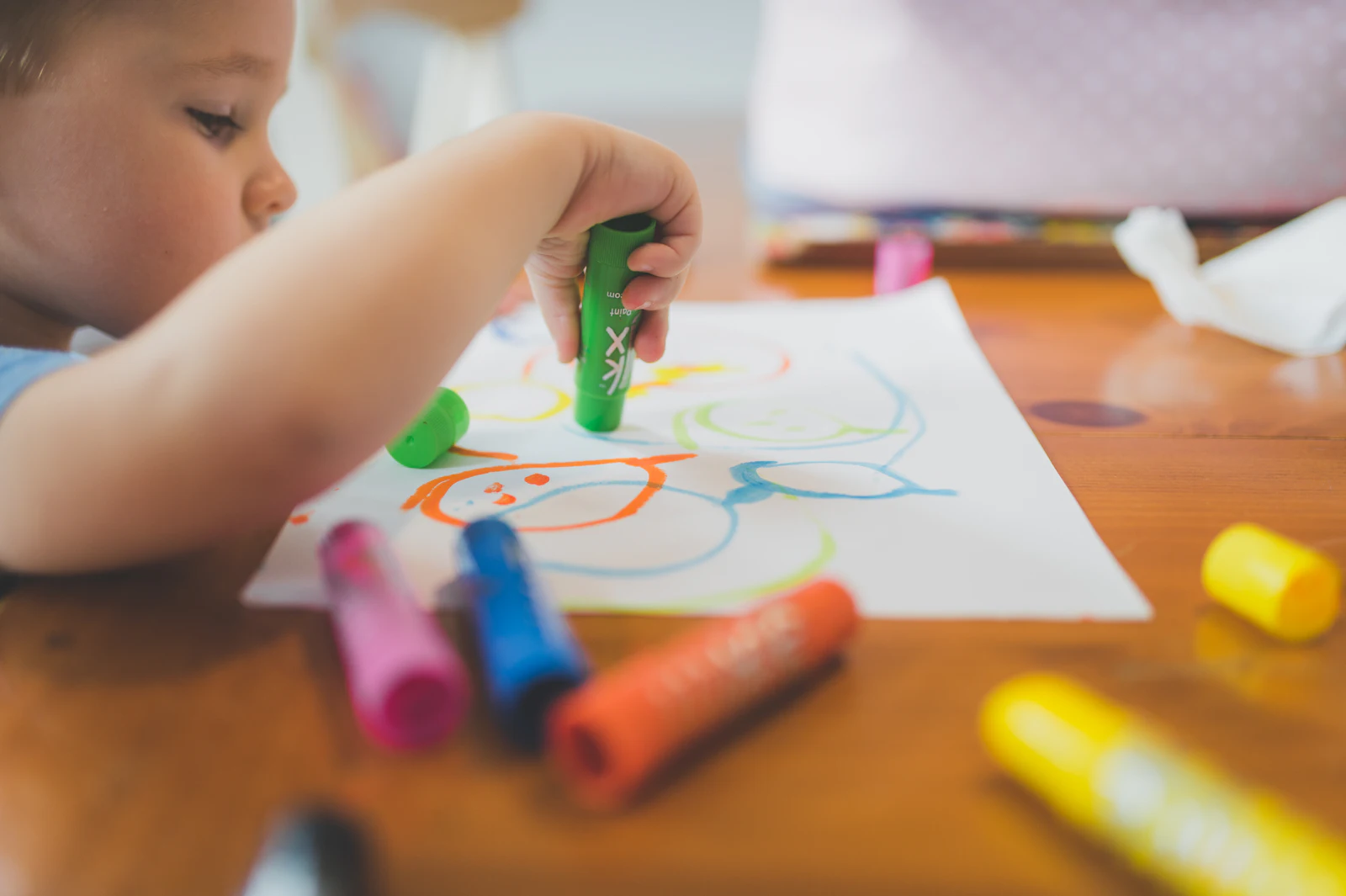 Un enfant dessine avec des feutres colorés sur une table en bois