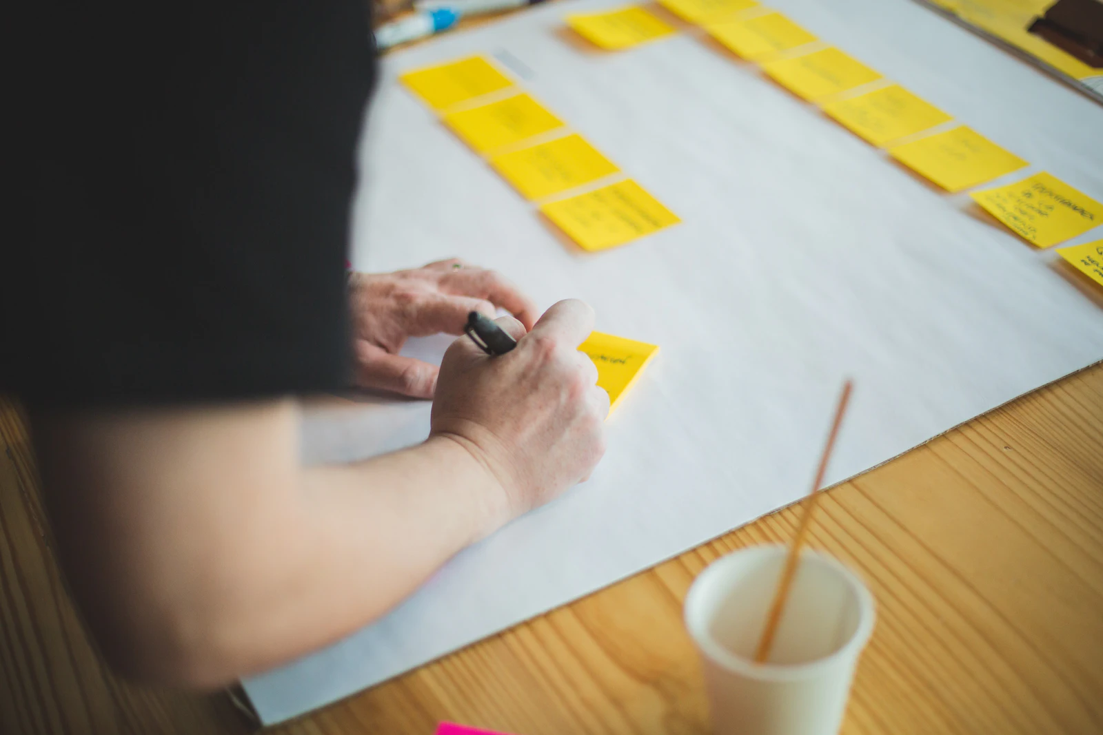 Une main écrit sur des notes adhésives, à côté d’une tasse