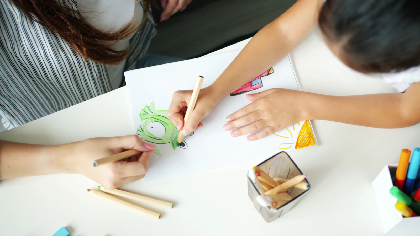 Les mains d’un adulte et d’un enfant qui dessinent ensemble