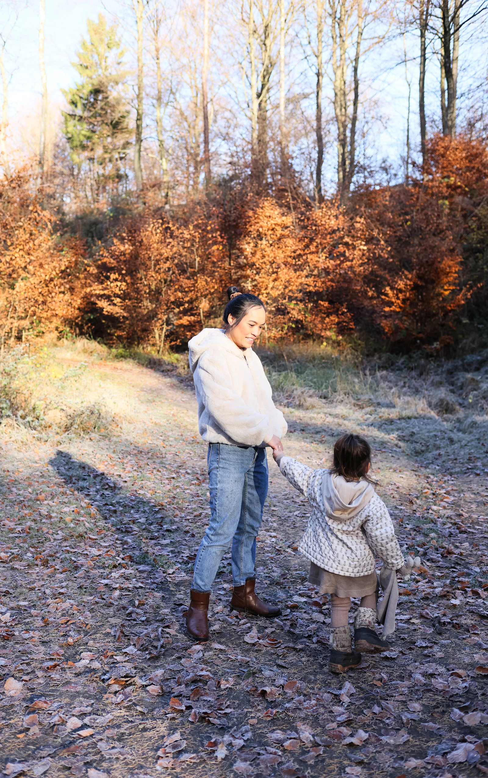 Une maman et son enfant marchent main dans la main sur un chemin de forêt en automne