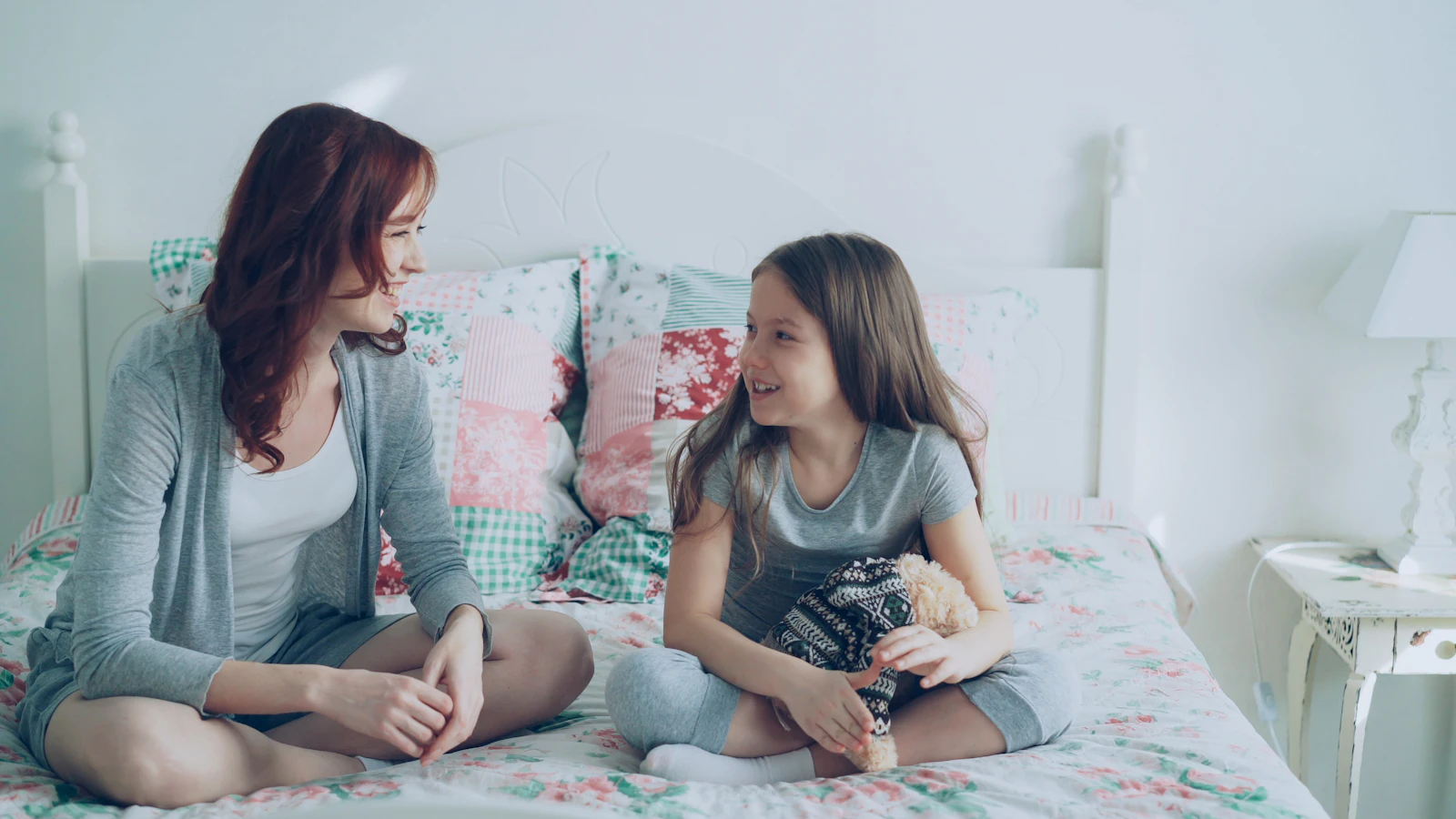 Une maman et sa fille discutent, assises sur un lit