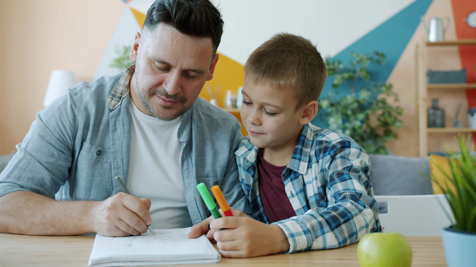 Un papa et son fils font les devoirs ensemble en souriant