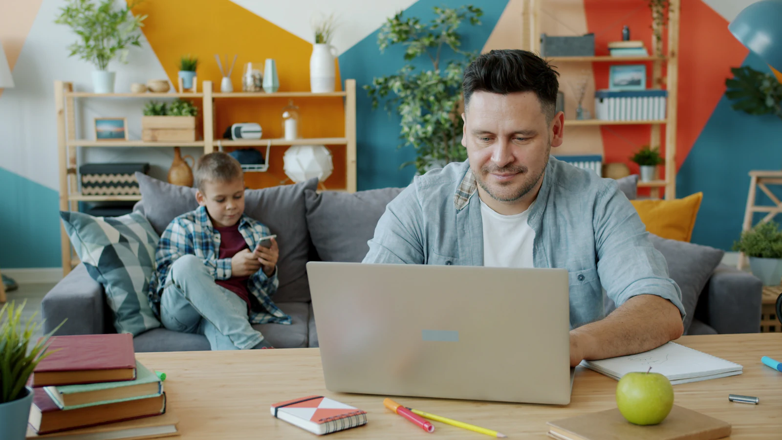 Un papa travaille sur son ordinateur pendant que son fils regarde un téléphone